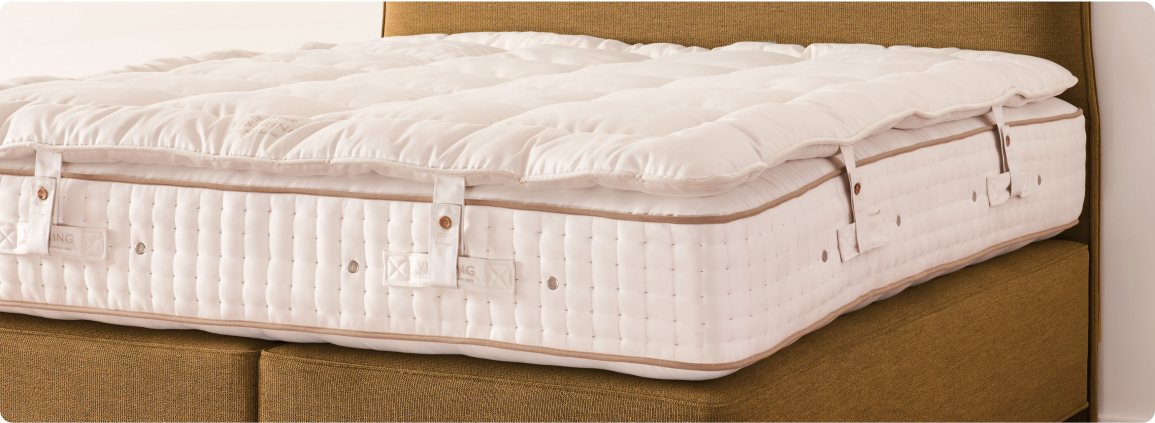 A luxury Vispring mattress topper laid out and secured to a white mattress on top of a mustard brown headboard and divan set